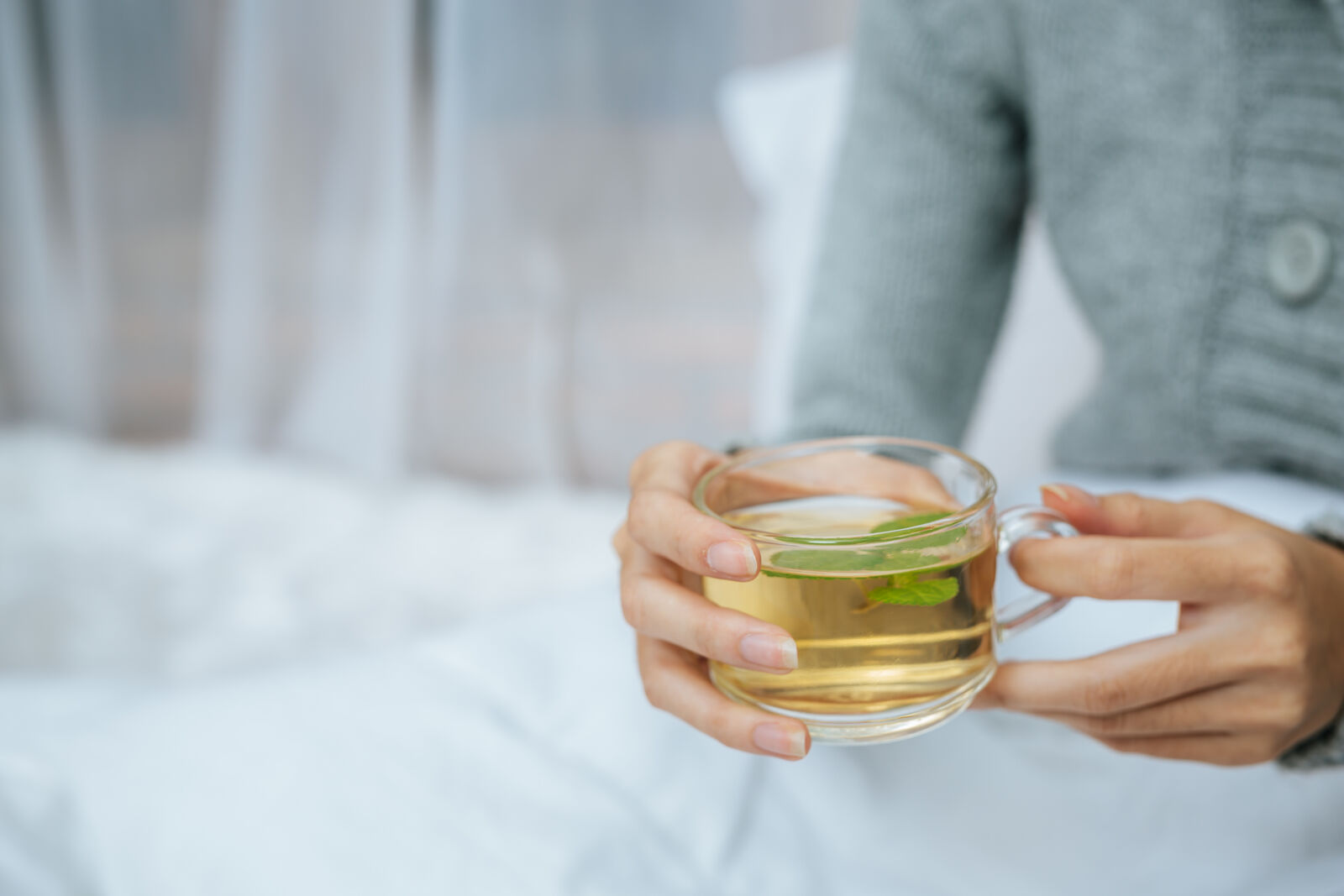 Hands holding a glass cup of herbal tea